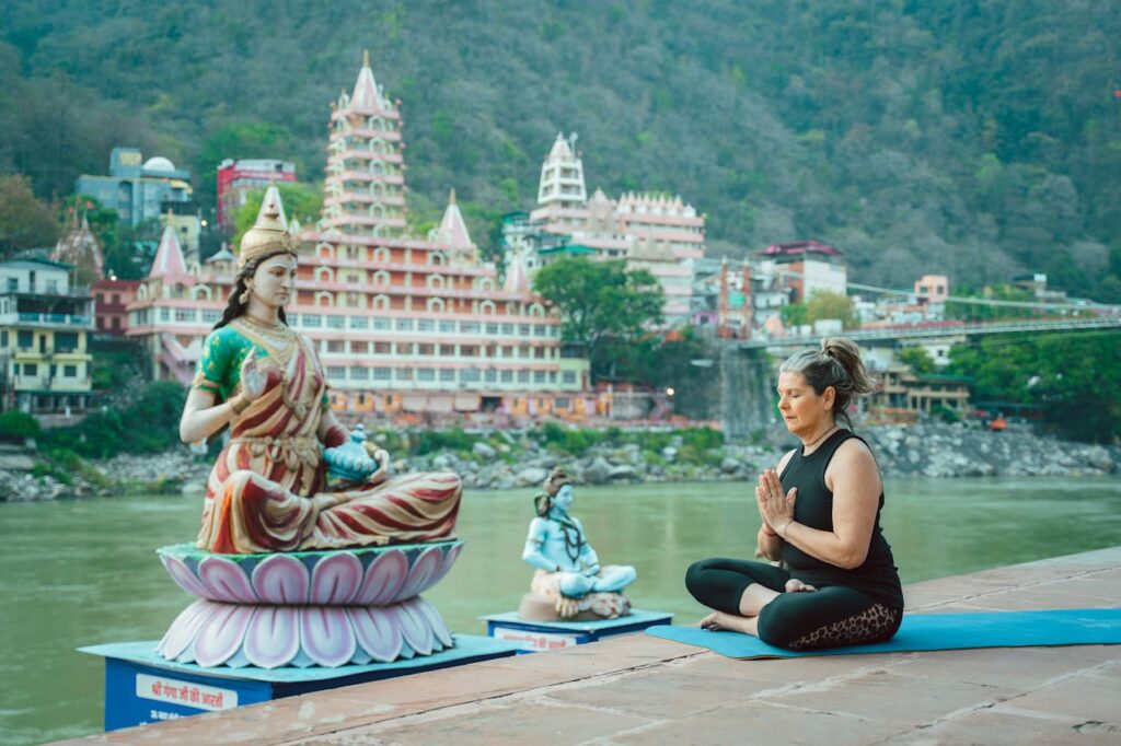 Woman meditating beside a statue by the Ganges in Rishikesh, capturing spirituality and serenity.