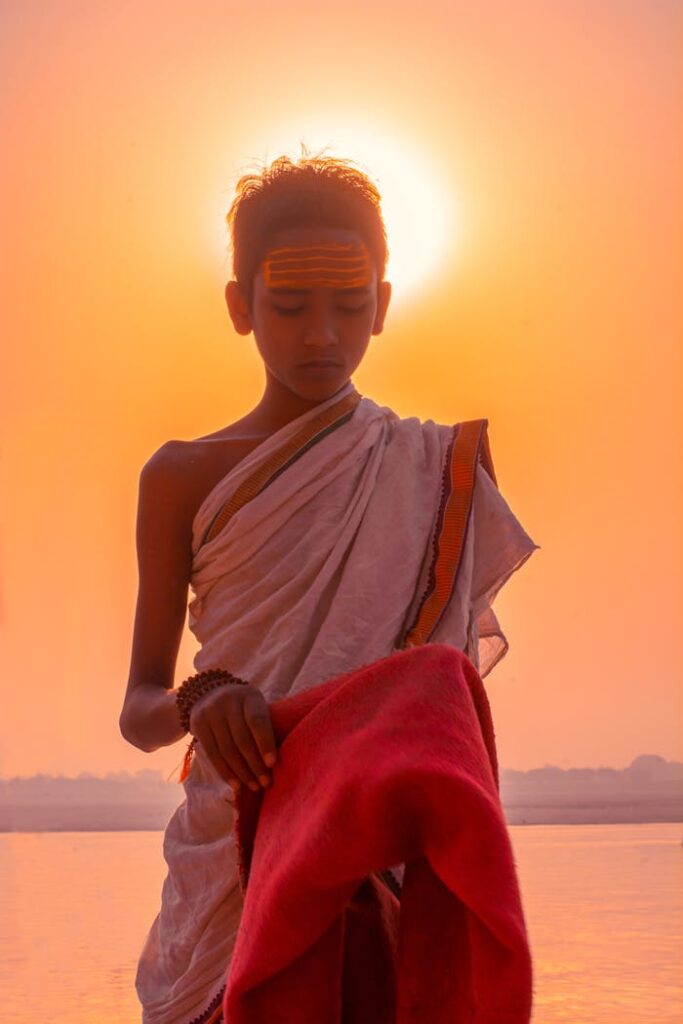 A young Indian priest performing a traditional ritual by the riverside in Varanasi at sunrise.